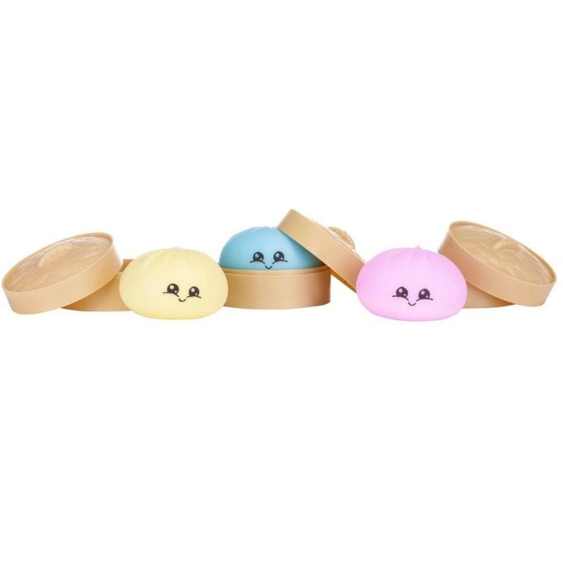 Four small round pastel items with cute face details, each resting on or beside a tan oval lid, arranged on a plain white background.